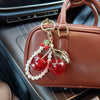 A brown leather handbag with a gold key chain featuring a red cherry and white pearl beads.