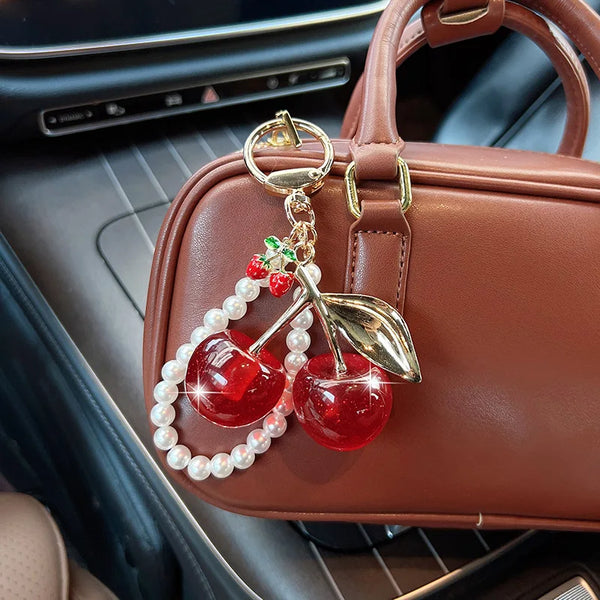 A brown leather handbag with a gold key chain featuring a red cherry and white pearl beads.