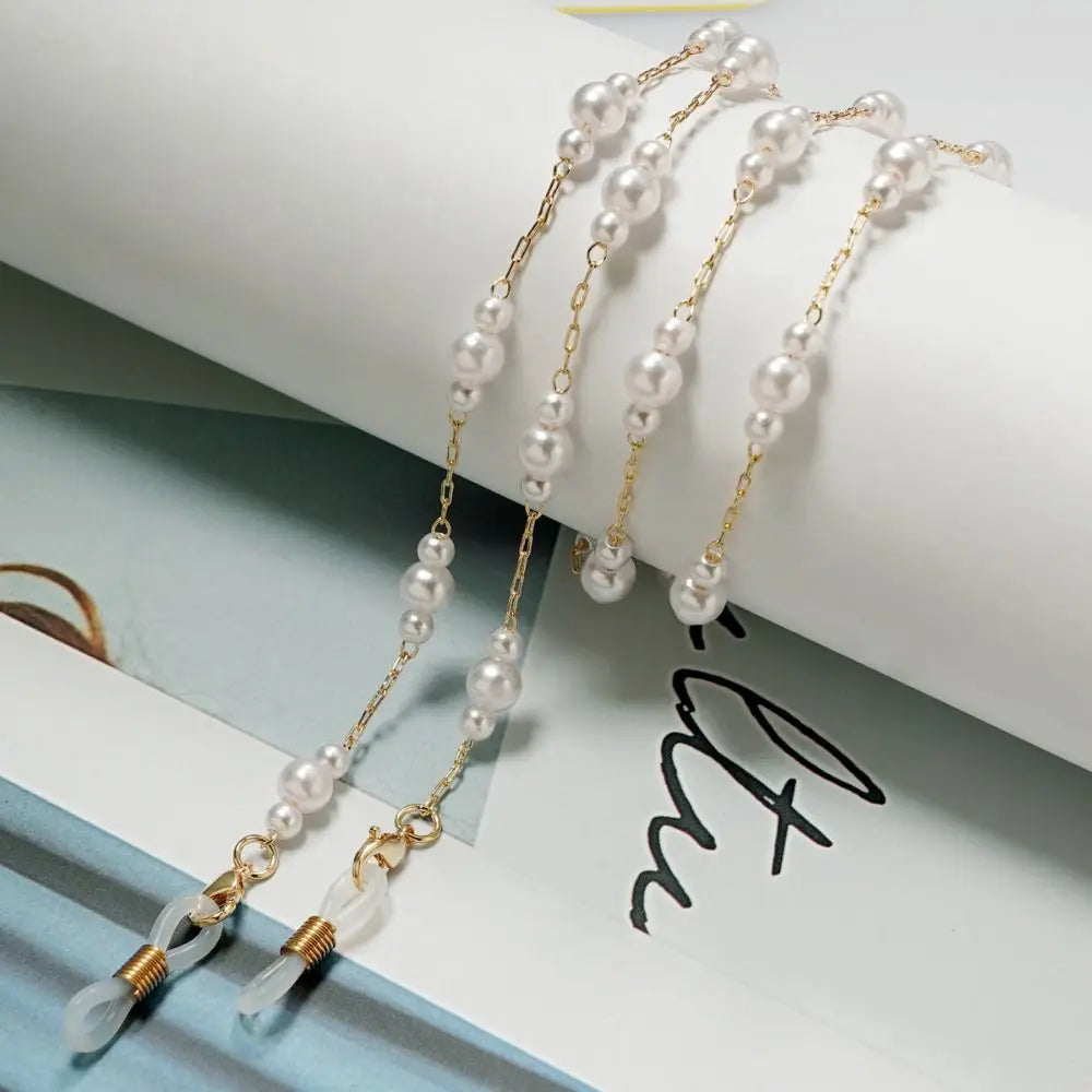 Collares para gafas de perla y cuentas tono dorado exhibidos sobre un fondo claro.