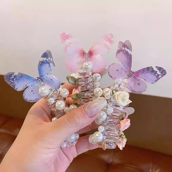 A hand holds a decorative arrangement of purple and pink fairy butterfly hair ropes adorned with pearls and floral elements.