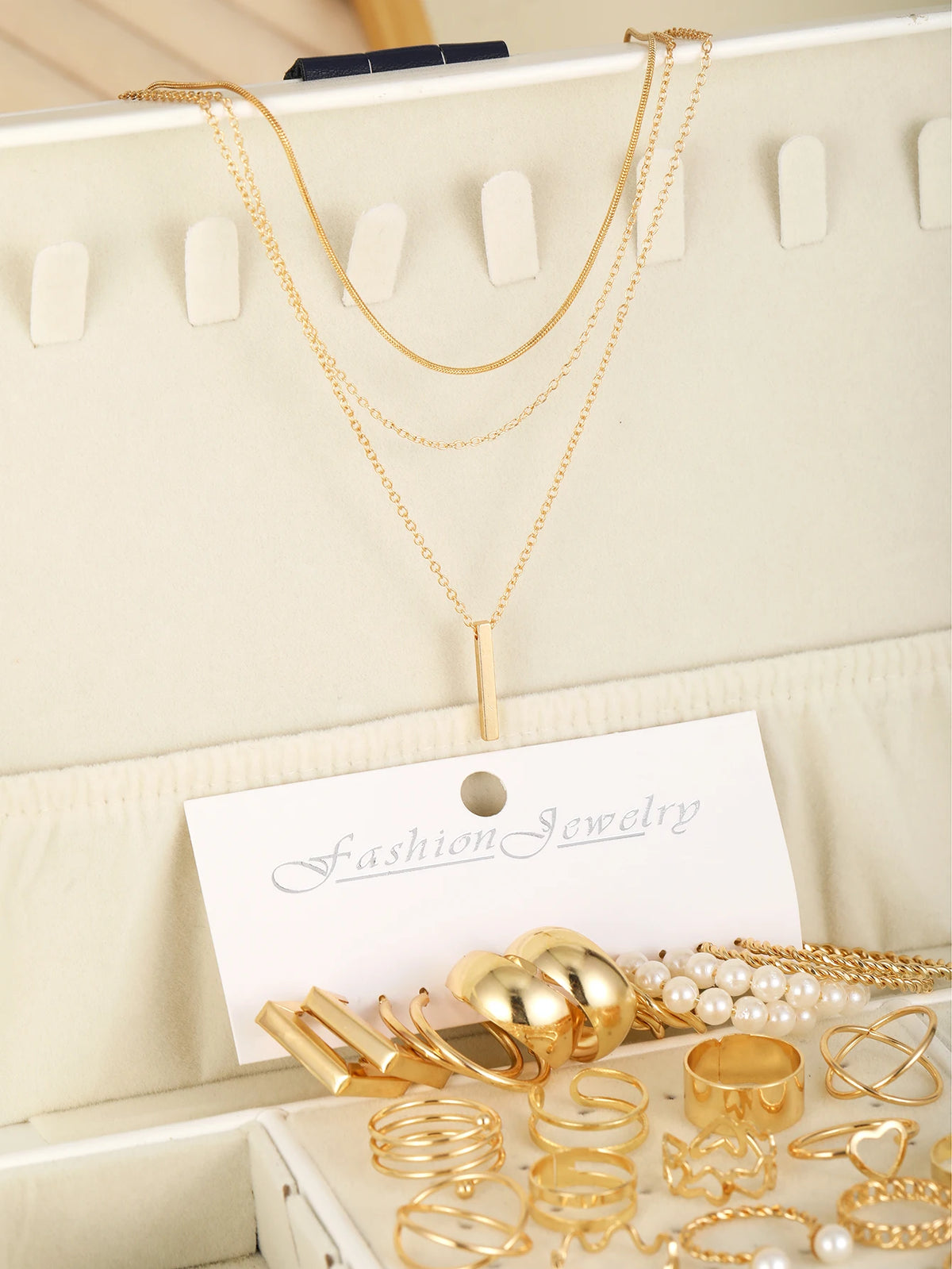 Un ensemble de bijoux géométriques dorés, incluant des colliers et des bagues superposés, présentés sur une carte blanche.