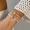A close-up of a hand wearing a stack of delicate pearl and beaded bracelets on the wrist.