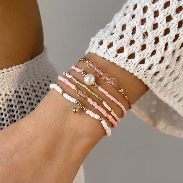A close-up of a hand wearing a stack of delicate pearl and beaded bracelets on the wrist.