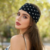 A woman wearing a black polka dot stretch hairband and a white top outdoors.