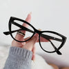 Eine Hand hält eine schwarze Vintage-Katzenauge-Lesebrille mit klaren Linsen vor weißem Hintergrund.