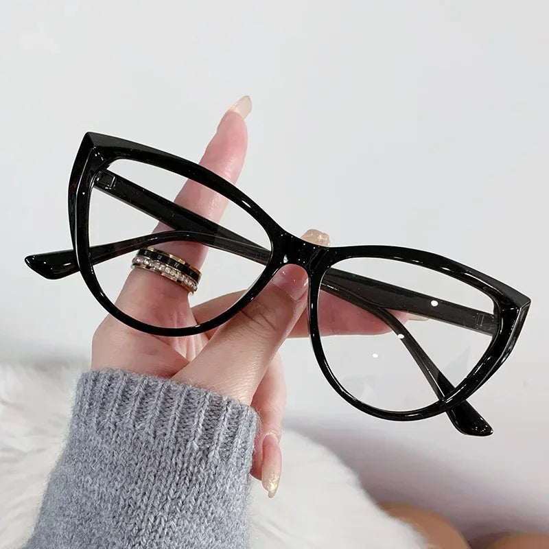 Eine Hand hält eine schwarze Vintage-Katzenauge-Lesebrille mit klaren Linsen vor weißem Hintergrund.