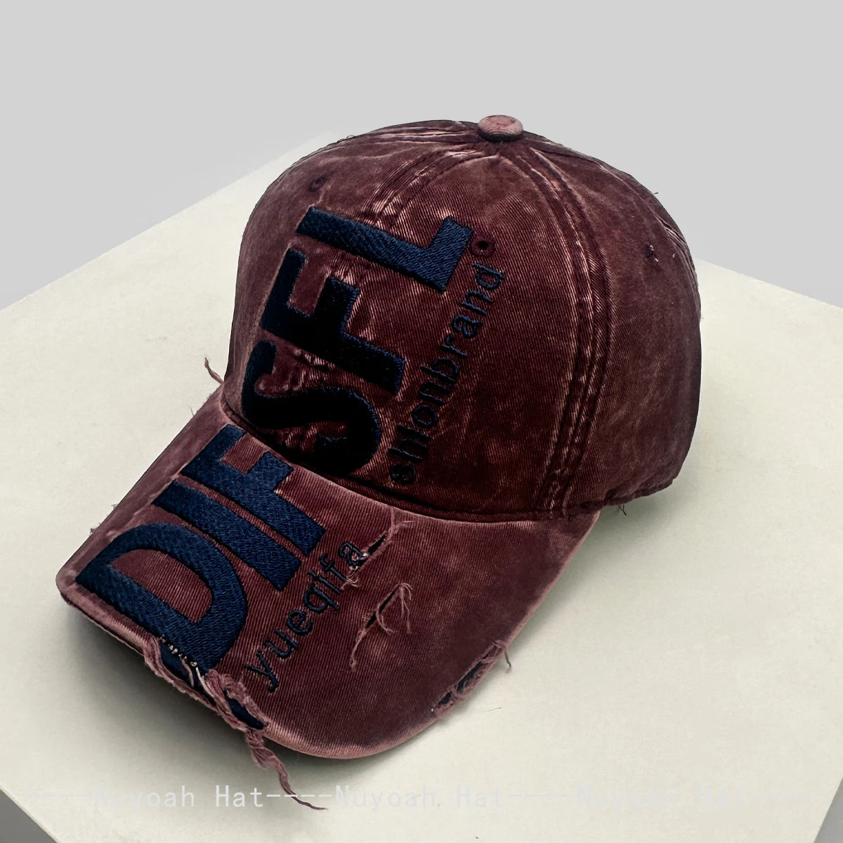 A dark brown velvet embroidered letter baseball cap with blue lettering resting on a white surface.