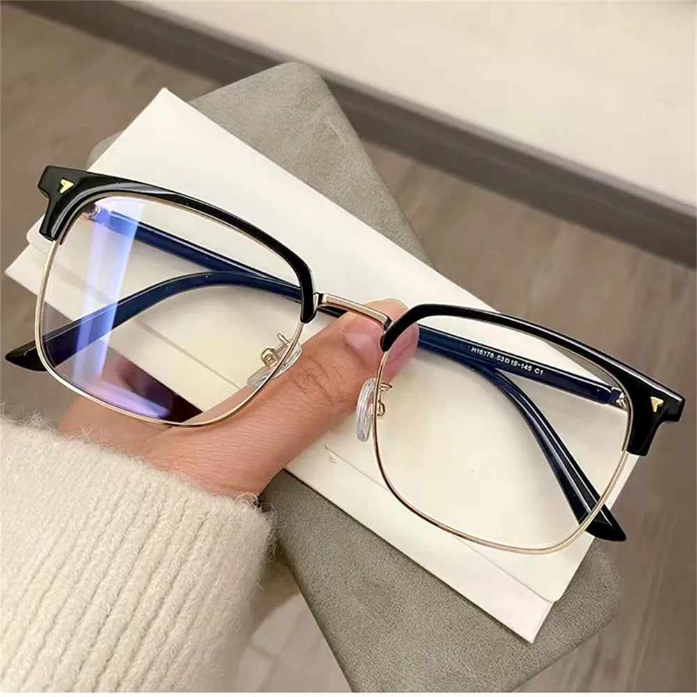 A close-up of clear anti-blue light eyeglasses resting on a white paper next to a person's hand.