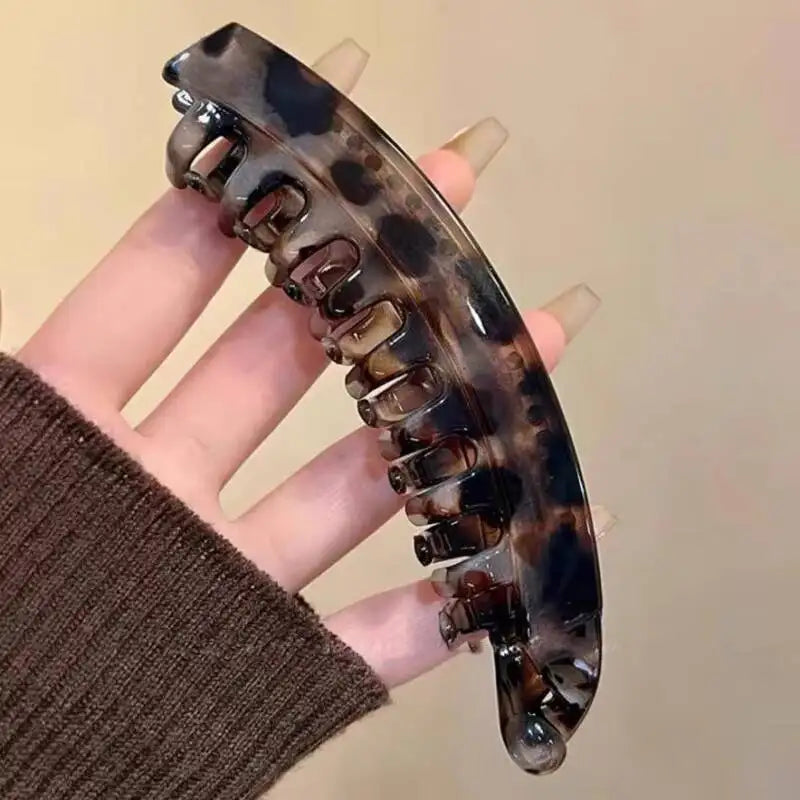 Eine Hand hält einen Schildpatt-Bananen-Haarspieß und eine Haarspange mit glänzendem, fleckigem Muster.
