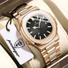 Nahaufnahme einer goldfarbenen Uhr mit Lederarmband und einem weißen Etikett auf einer hellbeigen Oberfläche.