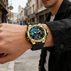A close-up of a men's wrist wearing a gold-toned sports watch with a black strap and blue face in an outdoor setting.