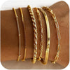 A stack of dainty gold plated bracelets on a brown wrist.
