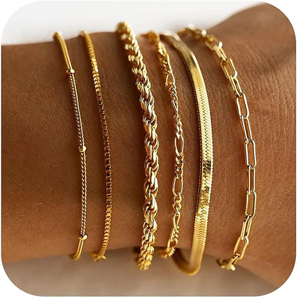 A stack of dainty gold plated bracelets on a brown wrist.