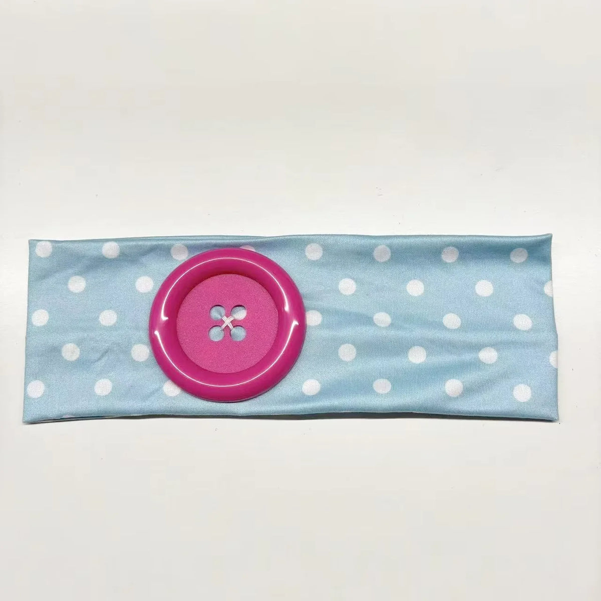 A pink fabric headband with white polka dots and a round button detail.