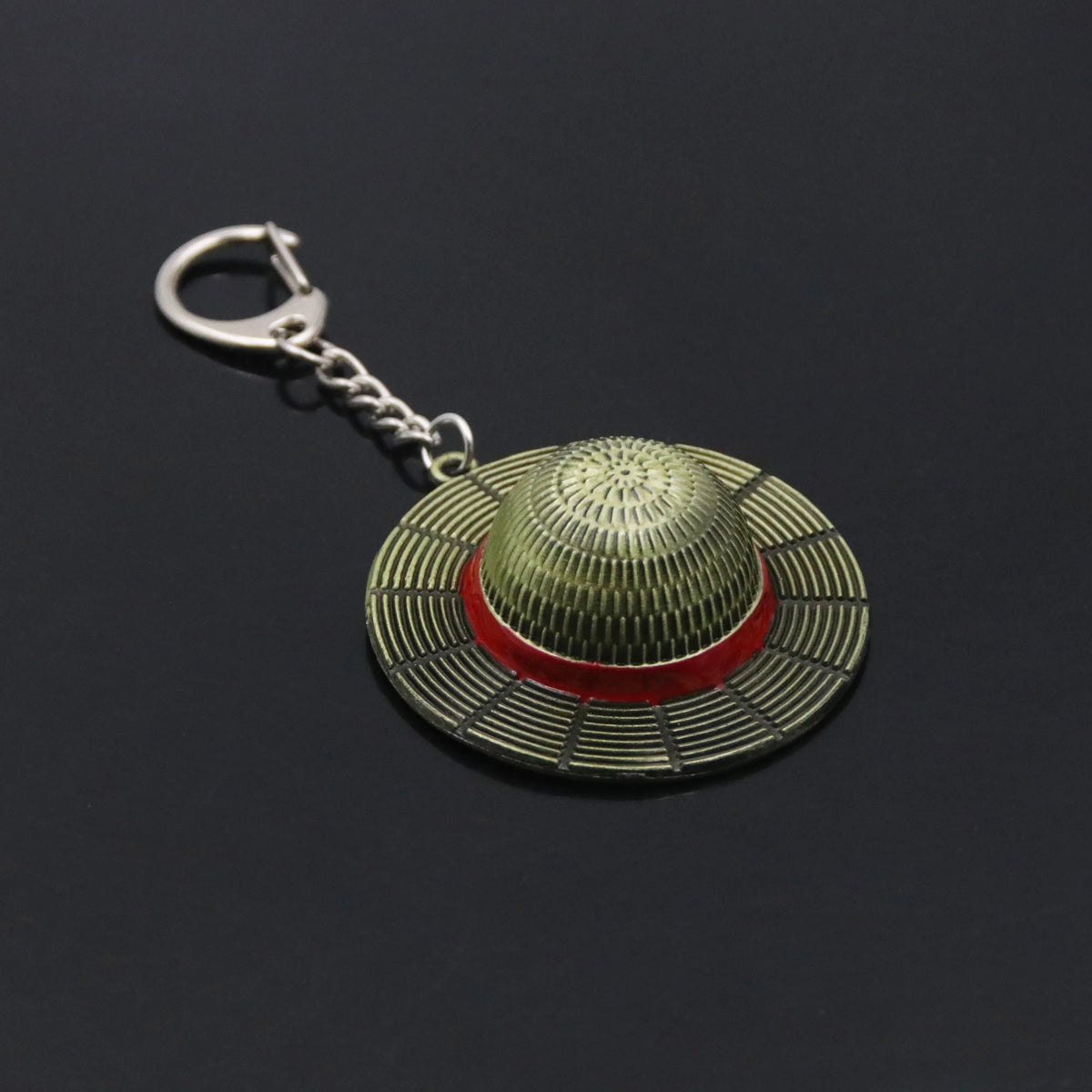 A metal keychain featuring an anime style straw hat with a green and red striped pattern.