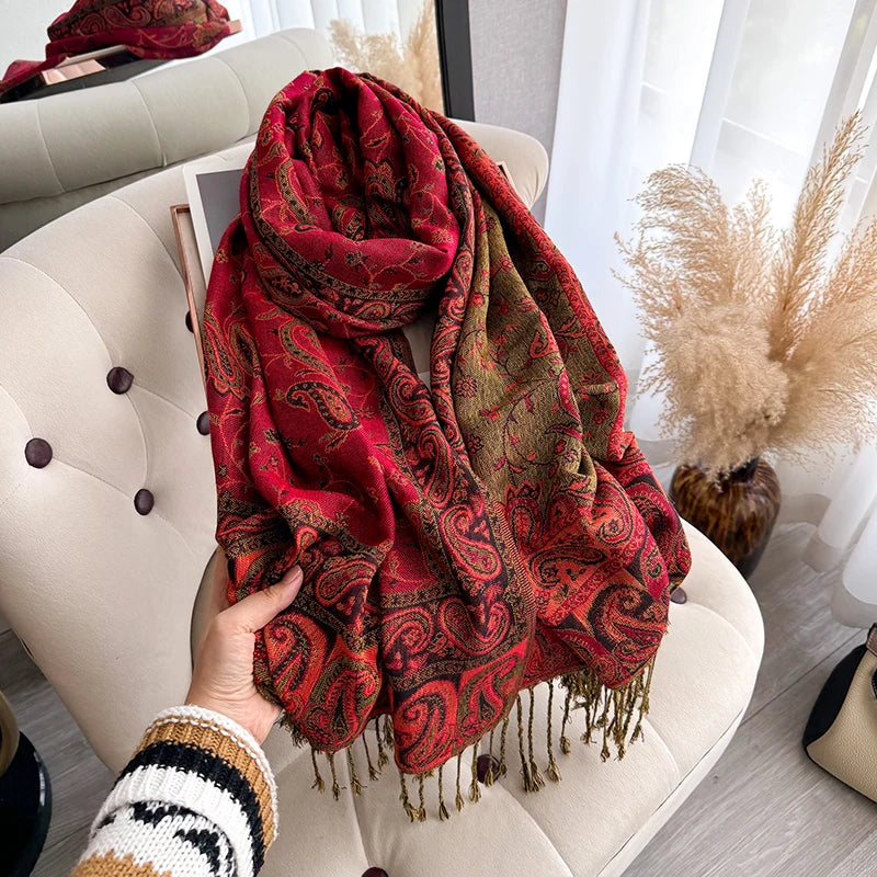 A vibrant red and gold bohemian paisley tassel shawl draped over a light beige sofa.