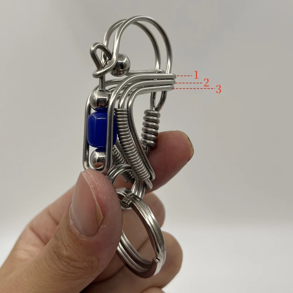 Un porte-clés mécanique en acier inoxydable avec une perle bleue et un fil enroulé tenu dans une main.