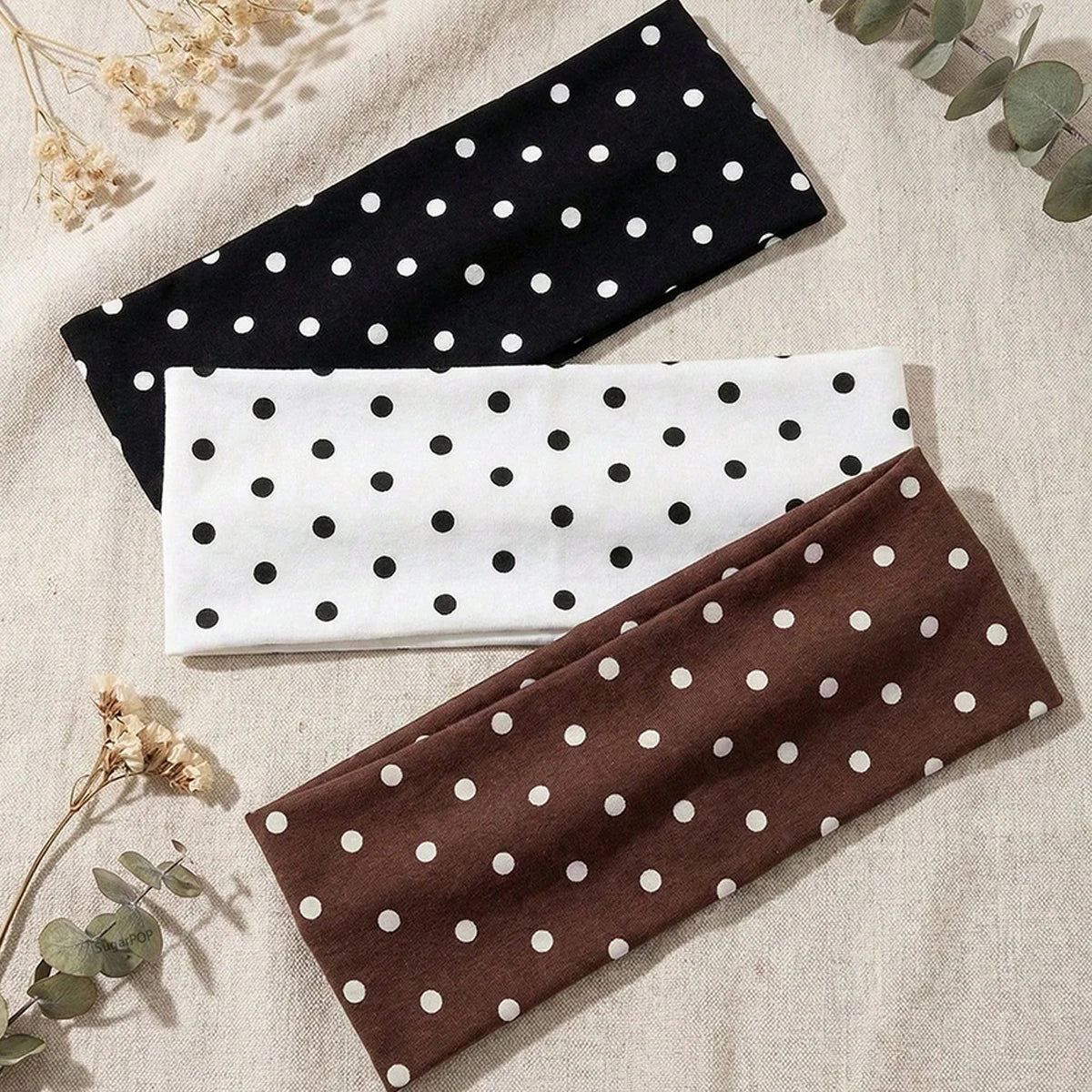 Trois bandeaux de sport noirs, blancs et marron à pois, sur un fond de tissu clair.