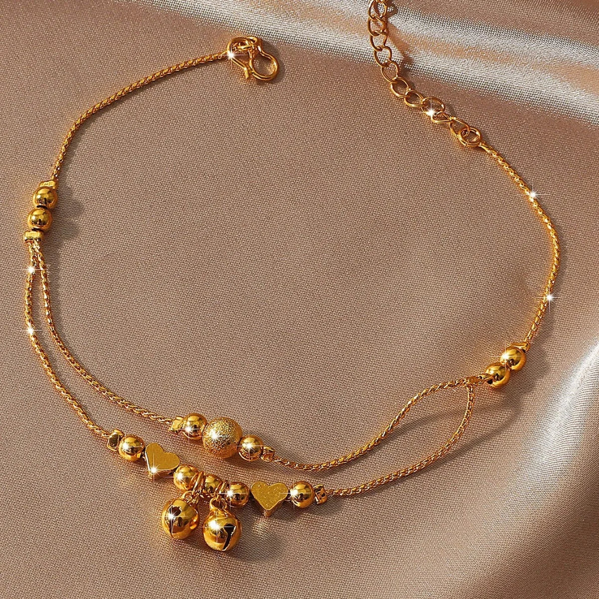 Gold-plated heart bell anklet for women displayed on a neutral fabric background.