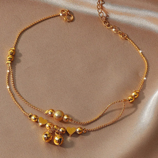 Gold-plated heart bell anklet for women displayed on a neutral fabric background.