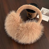 A beige faux fur earmuff with a dark container is shown on a wooden surface.