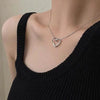 A silver heart-shaped necklace with a delicate chain worn around the neck against a black top.