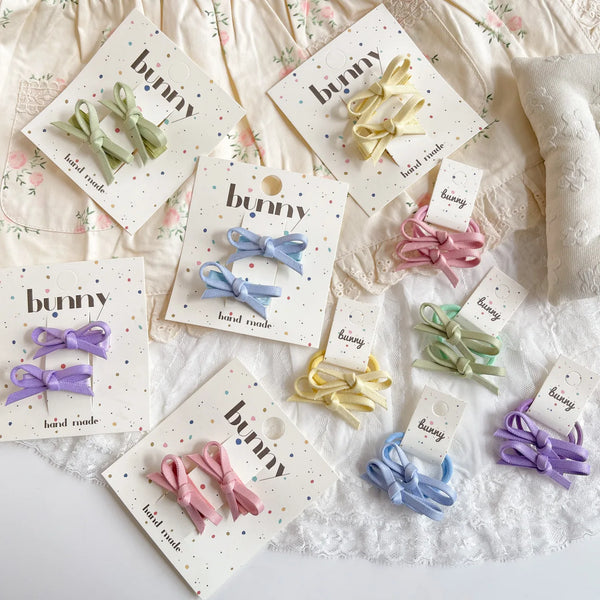 A collection of handmade bowknot hair clips in various pastel colors like pink, purple, and mint green displayed on white pap
