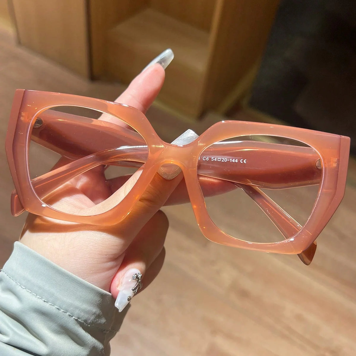 A hand holds a pair of translucent orange-colored fashion glasses with large frames.