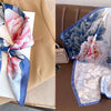 A light blue floral print silk scarf tied in a bow displayed on a tan blazer.