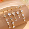 A set of five gold stainless steel dangled belly button rings with clear and white stones displayed on a beige surface.