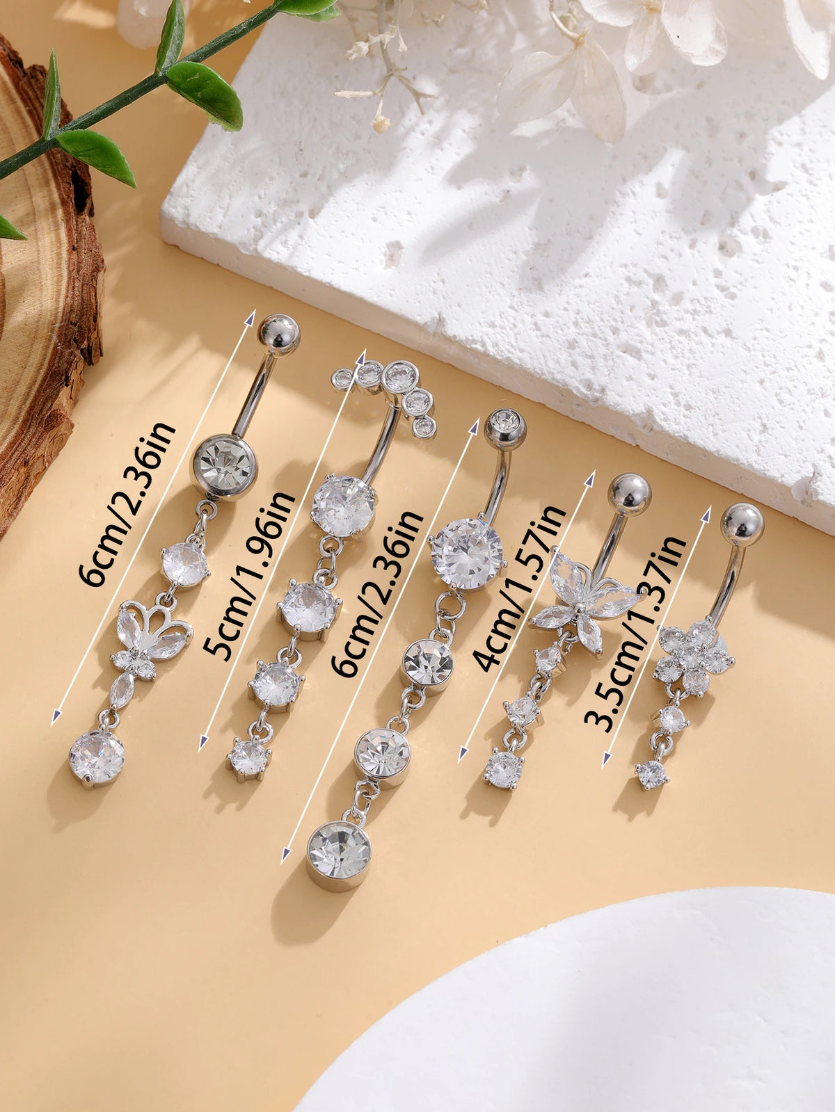 A set of five gold stainless steel dangled belly button rings with various gemstone sizes displayed on a light background.