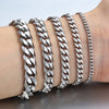 A wrist displays several silver stainless steel Cuban link bracelets stacked together.