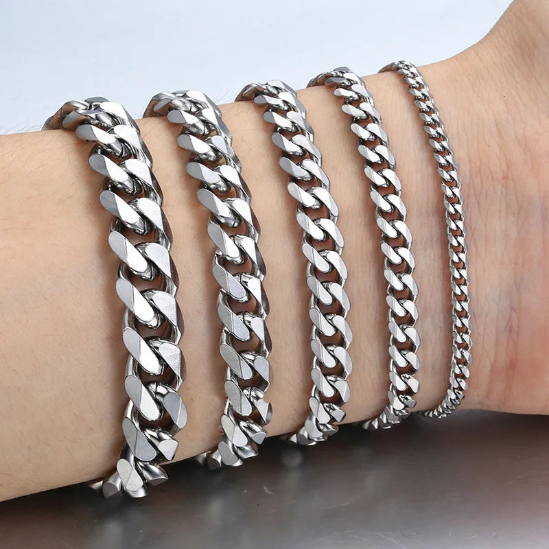 A wrist displays several silver stainless steel Cuban link bracelets stacked together.