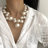 A close-up of an elegant simulated pearl choker necklace worn against a white blouse.