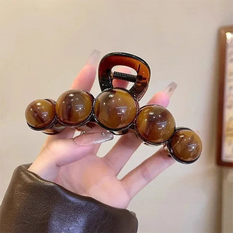 Eine Hand hält eine retro, gradientierte Perlen-Haarklammer mit dunklen Bernsteinperlen vor hellem Hintergrund.