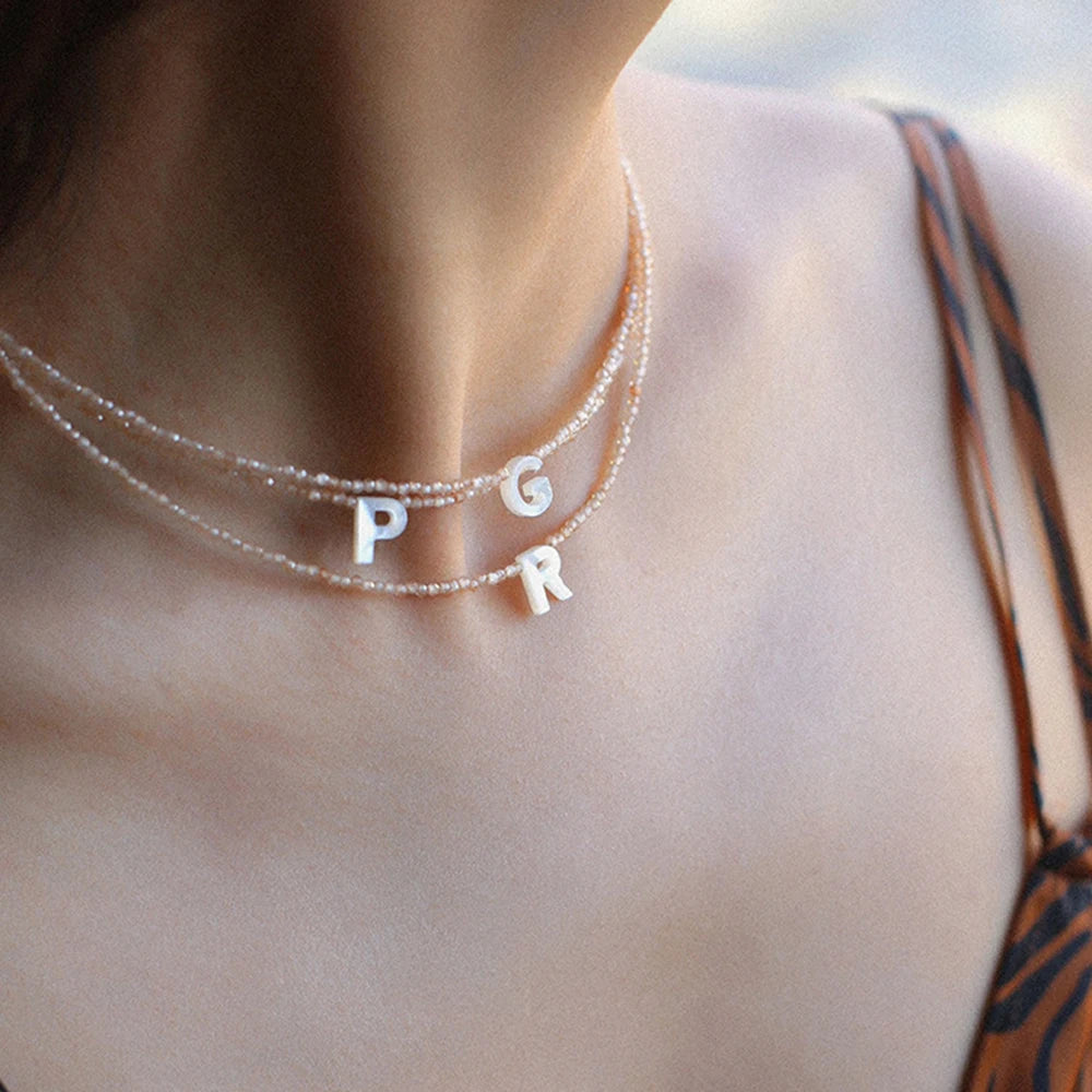 A close-up of a delicate pearl necklace spelling out P G R on a woman's neck.
