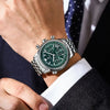 Un reloj cronógrafo de lujo para hombre con esfera verde y caja de plata, llevado en la muñeca junto a una chaqueta de traje.