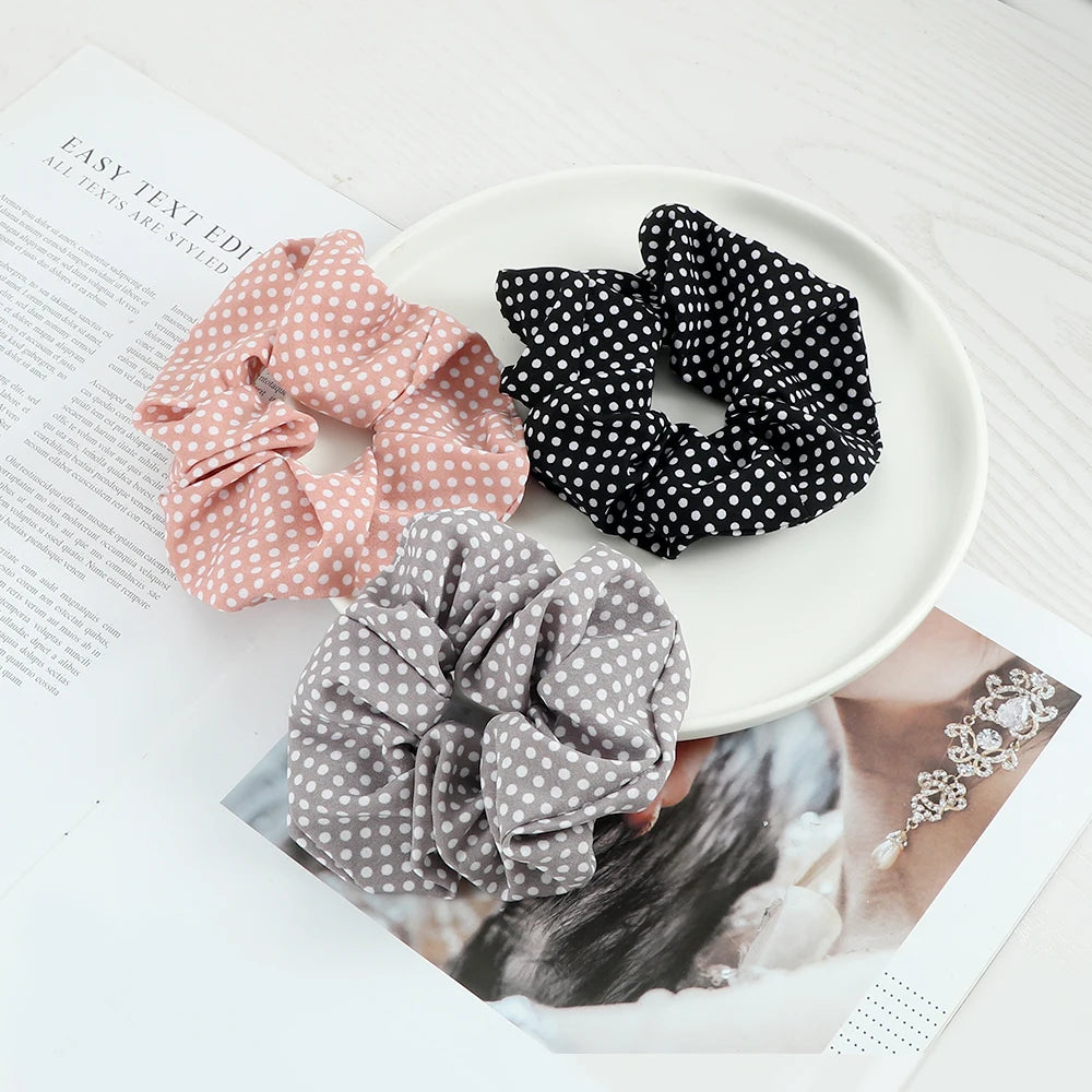A display of three knitted hair scrunchie headbands in pink, black polka dots, and gray polka dots on a white plate.