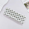A white fabric headband with black polka dots is displayed on a light surface.