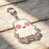 A clear, cute ghost-shaped keychain charm with pink and white details resting on a wooden surface.
