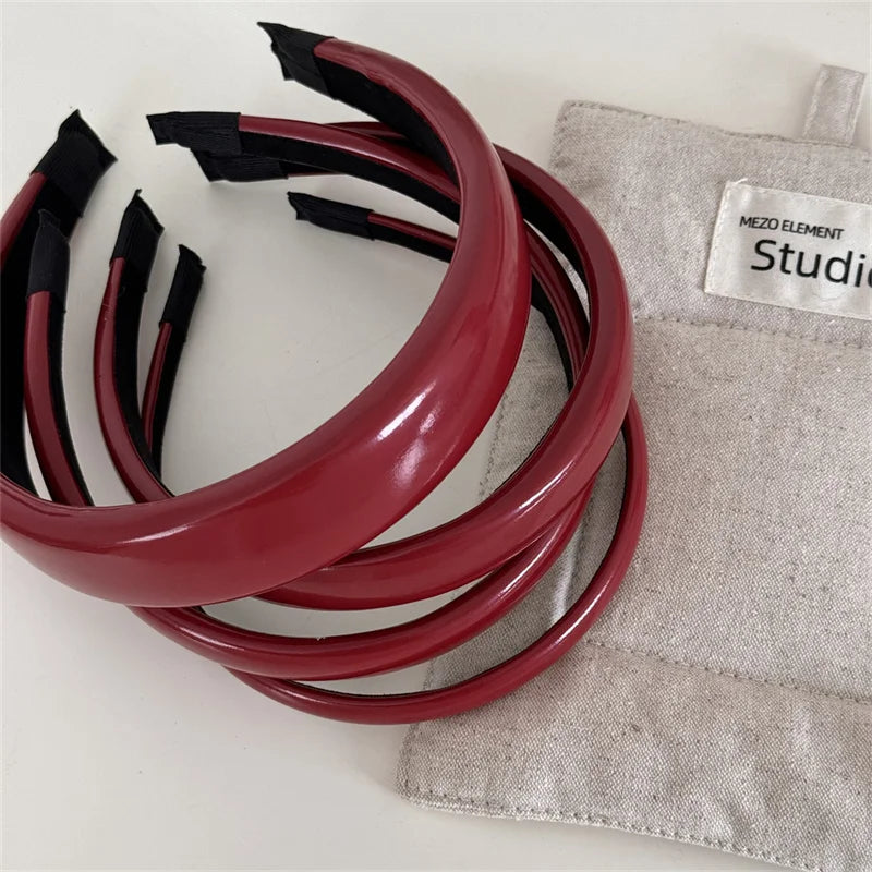 A set of maroon PU leather fashion headbands rolled up on a beige cloth with a label.