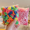 A hand holds a clear plastic bag filled with colorful elastic hair bands for girls.