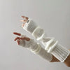 A hand wearing white fingerless arm warmers, showing the knitted texture and fit.