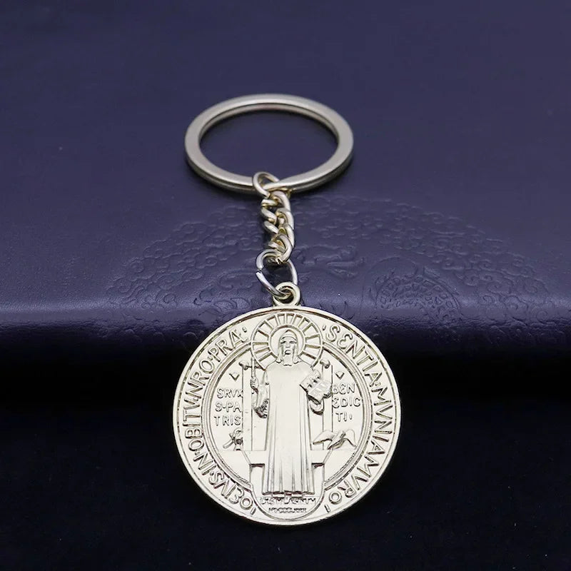 Silver round medallion keychain featuring a religious figure and text on a dark blue background.