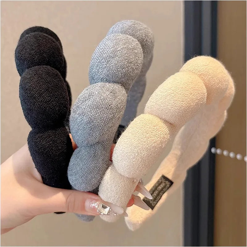 A hand holds a set of cloud sponge hair accessories headbands in black, gray, and cream colors.