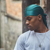 Un hombre vistiendo un turbante bandana de seda color verde azulado y una camiseta gris claro.