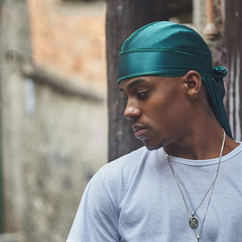 Un hombre vistiendo un turbante bandana de seda color verde azulado y una camiseta gris claro.