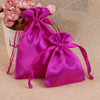 A vibrant magenta satin drawstring pouch with pink flowers is displayed on a beige fabric background.