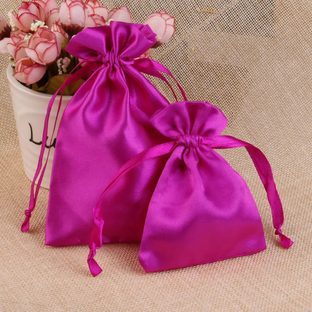 A vibrant magenta satin drawstring pouch with pink flowers is displayed on a beige fabric background.