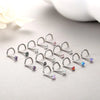 A collection of surgical stainless steel nose piercing studs with various colored gemstones arranged on a light gray surface.